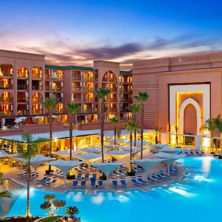 ซาวอย เลอ กร็อง โฮเต็ล มาราเกช Hotel มาร์ราเกช ภายนอก รูปภาพ The photo shows a luxurious hotel resort situated near a large swimming pool. The architecture features traditional Moroccan elements, with a prominent entrance that has arched designs. Surrounding the pool are numerous lounge chairs, and palm trees 