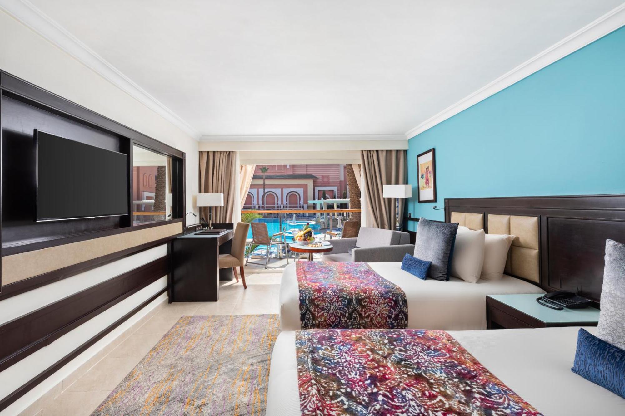 ซาวอย เลอ กร็อง โฮเต็ล มาราเกช Hotel มาร์ราเกช ภายนอก รูปภาพ The photo shows a stylish hotel room featuring two beds, each adorned with colorful patterned bedspreads. The walls are painted in a calming blue hue, and there are large windows allowing natural light to fill the space, with a view of an outdoor poo