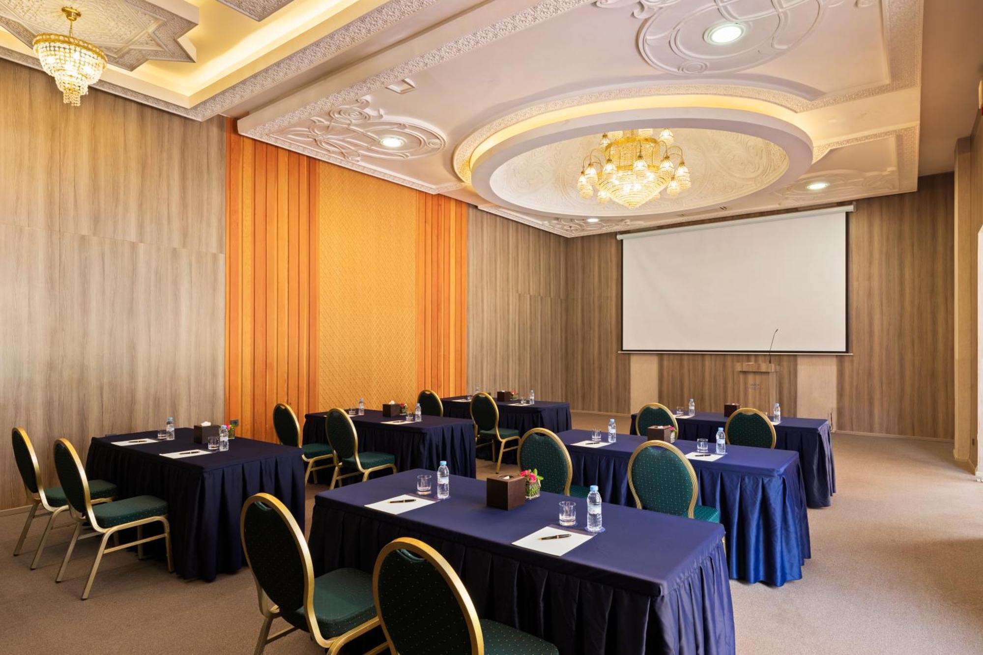 ซาวอย เลอ กร็อง โฮเต็ล มาราเกช Hotel มาร์ราเกช ภายนอก รูปภาพ The photo shows a conference or meeting room. It features several tables arranged in a classroom or seminar style, each covered with a dark blue tablecloth. There are green chairs positioned around the tables. On the tables, there are water bottles a