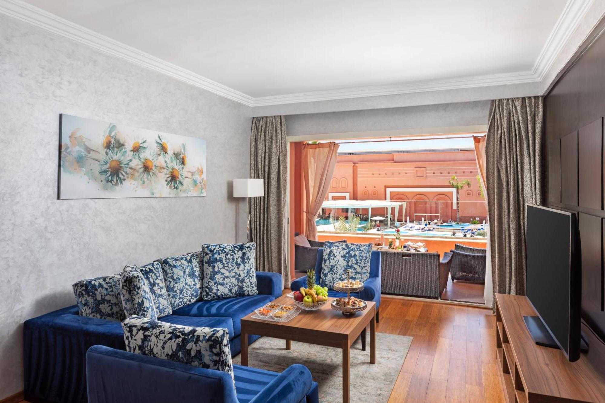 ซาวอย เลอ กร็อง โฮเต็ล มาราเกช Hotel มาร์ราเกช ภายนอก รูปภาพ The photo shows a bright and stylish living area. It features a comfortable seating arrangement with blue sofas adorned with floral patterns. A wooden coffee table sits in front of the sofas, while a flat-screen TV is positioned nearby. Large curtain