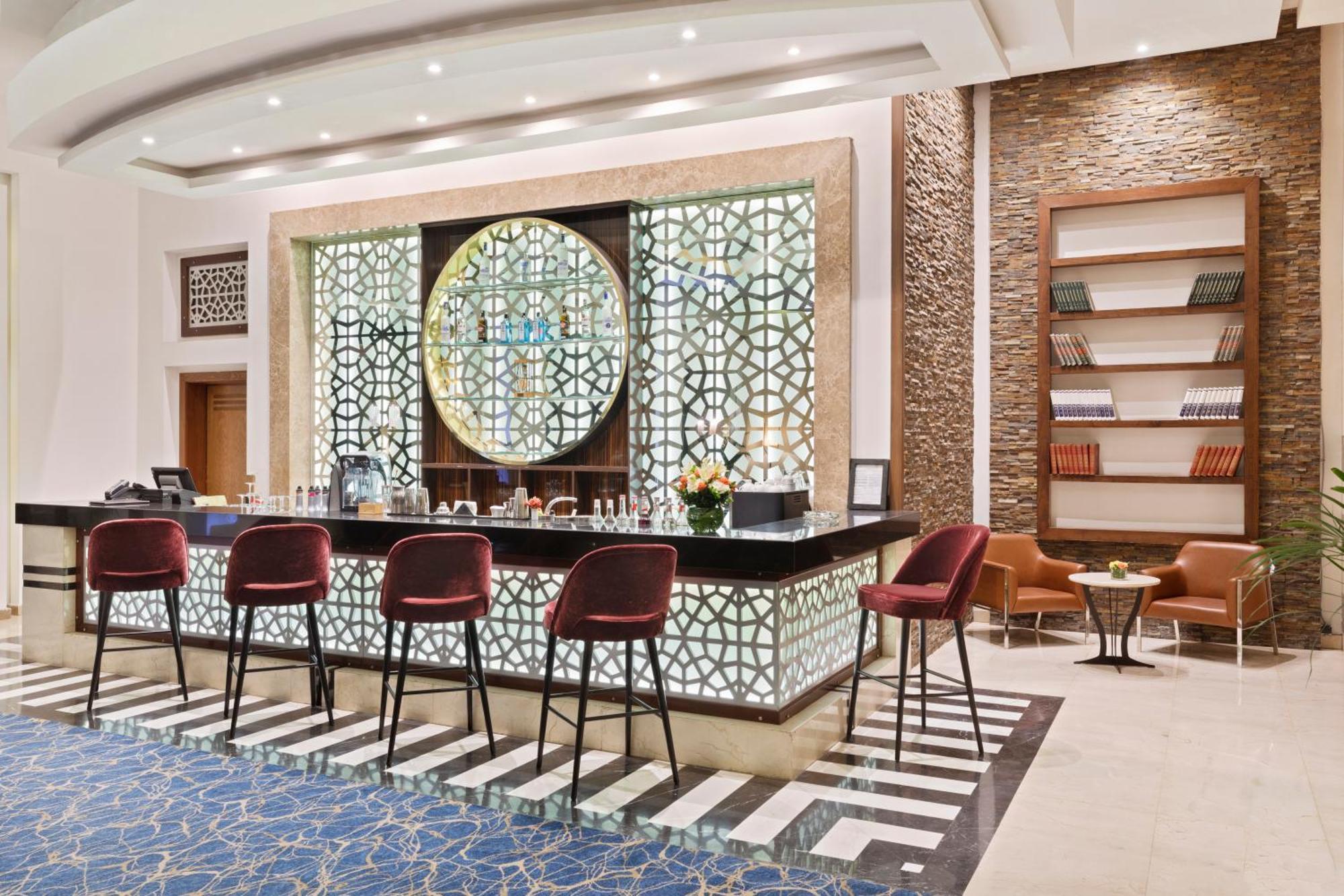 ซาวอย เลอ กร็อง โฮเต็ล มาราเกช Hotel มาร์ราเกช ภายนอก รูปภาพ The image shows an elegantly designed bar area within a hotel or lounge. The bar features a stylish countertop with several high chairs in a rich red color. Behind the bar, there’s a decorative wall featuring intricate geometric patterns, likely insp